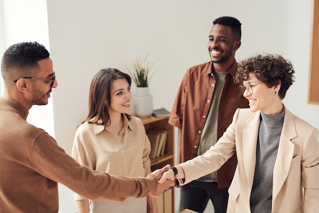 A group of four people greeting each other, two of them are shaking hands